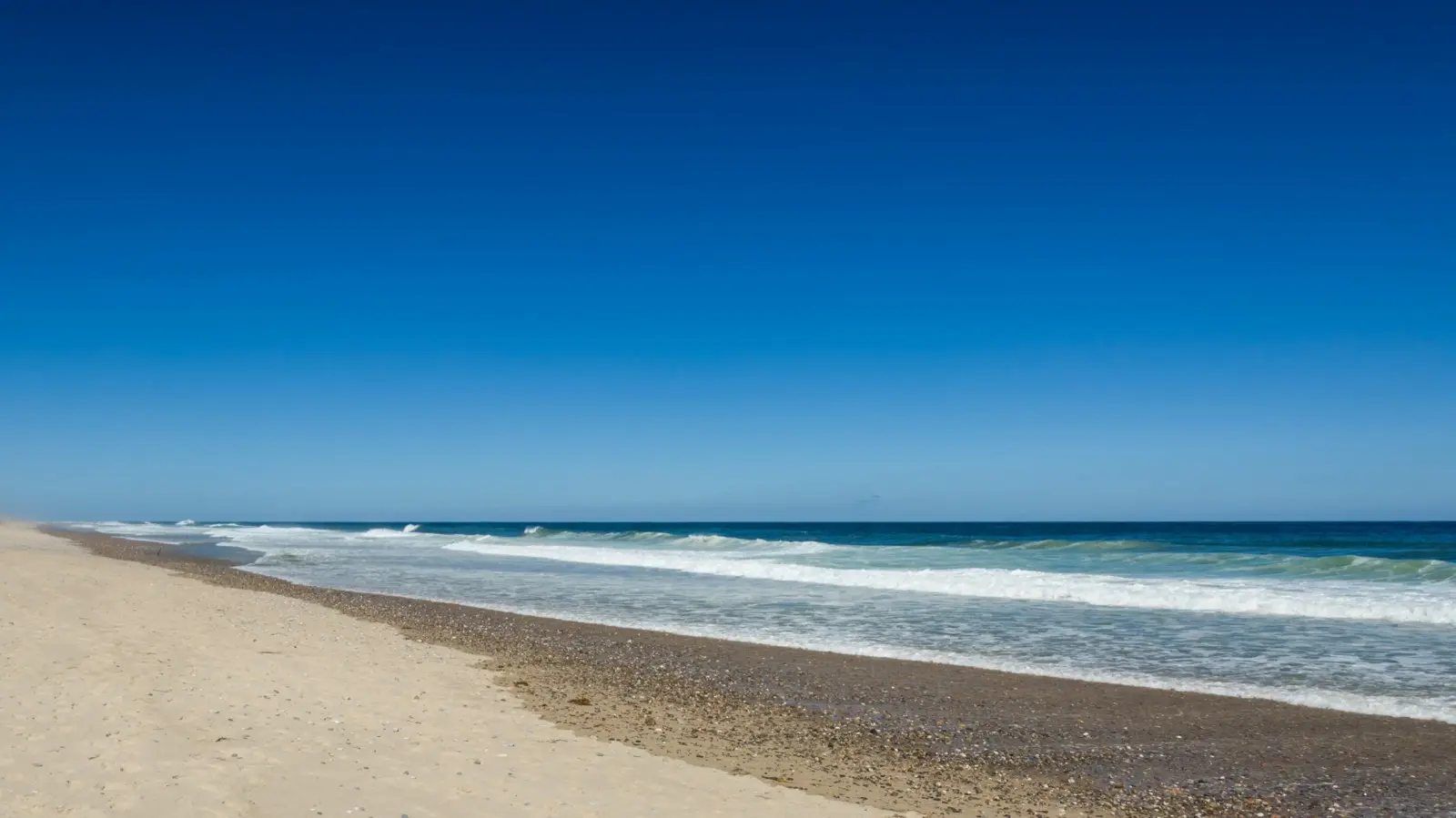 Waves rolling onto a Cape Cod beach under a clear blue sky